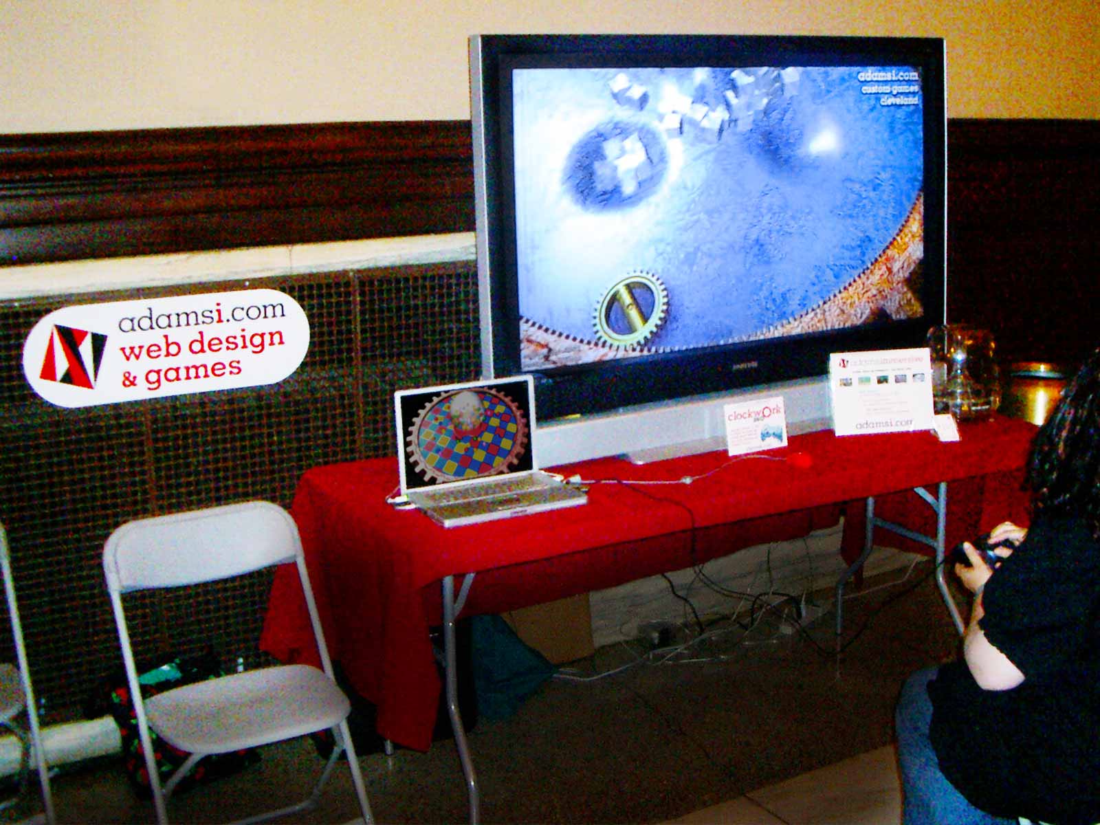 Photo: woman with gamepad playing Mac game on large screen at technology festival